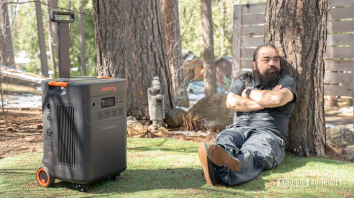 Visual Jackery Explorer 5000 Plus berwarna oranye hitam yang kokoh dengan roda, diletakkan di samping peralatan rumah tangga saat pemadaman listrik.