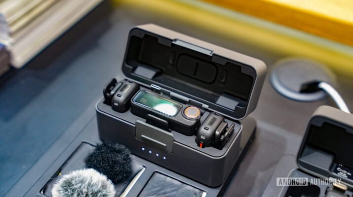 Satu set mikrofon nirkabel DJI Mic 3 berwarna hitam dengan casing pengisi daya terbuka, menampilkan dua transmitter mungil dan satu receiver yang siap dipasangkan ke kamera atau smartphone.