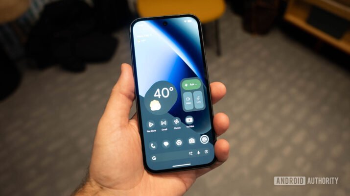 Smartphone Google Pixel 10a warna Obsidian dengan layar 120Hz yang menampilkan antarmuka Android 16 terbaru di atas meja kayu minimalis.