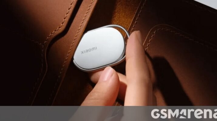 Visual produk Xiaomi Tag berwarna putih minimalis bersanding dengan gantungan kunci kulit di atas meja kayu, menunjukkan desain ringkas pelacak pintar terbaru Xiaomi.