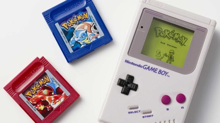 Miniatur Pokémon Jukebox Game Boy berwarna abu-abu klasik memainkan musik dari cartridge kecil di atas meja kerja kayu bergaya retro